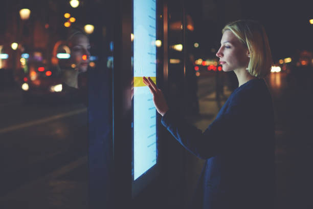 istock Young woman touching sensitive screen while selecting option on the list for find out schedule of city transport with smart stop bus in Barcelona, female standing at big display which reflecting light 908210392
