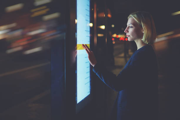 istock Young woman touching sensitive screen while selecting option on the list for find out schedule of city transport with smart stop bus in Barcelona, female standing at big display which reflecting light 908210448