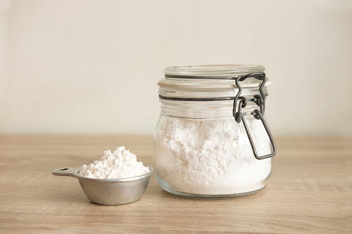 White flour in a measuring cup and transparent jar at the center on a wood table.