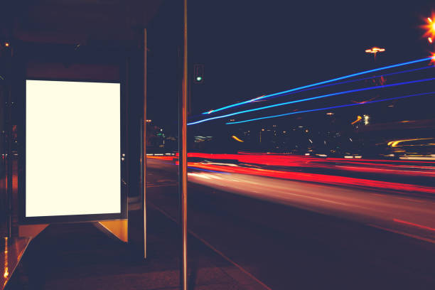 istock Blank electronic billboard with copy space for your text message or promotional content, public information board on bus stop, advertising mock up outdoors, empty poster in urban setting at night 908220104