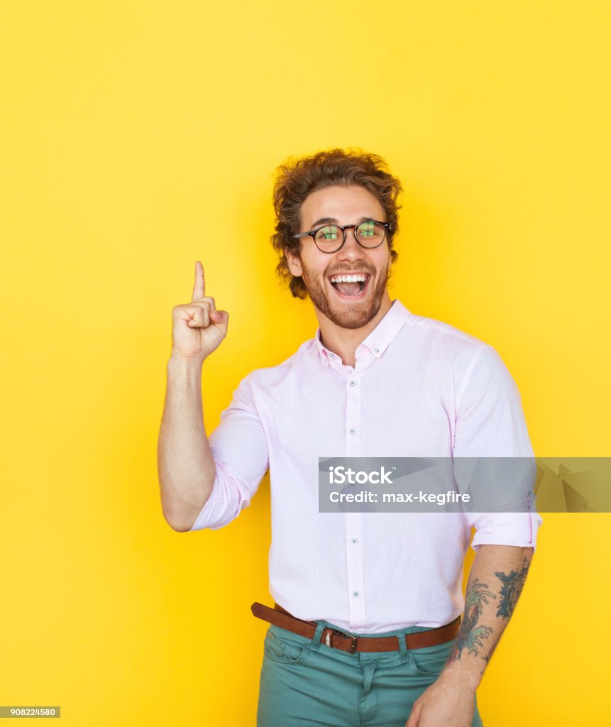 Young stylish man pointing up Handsome smart man in eyeglasses and white shirt pointing up on yellow looking excited. Men Stock Photo