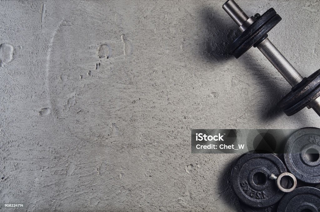 Fitness or bodybuilding background. Dumbbells on gym floor, top view Fitness or bodybuilding concept background. Product photograph of old iron dumbbells on grey, conrete floor in the gym. Photograph taken from above, top view with lots of copy space Gym Stock Photo