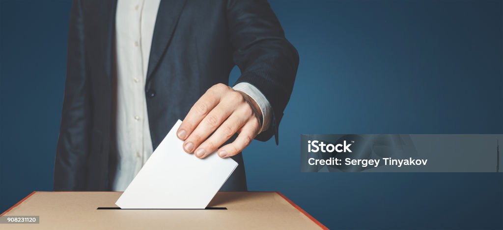 Man Voiter Putting Ballot Into Voting box. Democracy Freedom Concept Unrecognizable male voter holds in his hand a ballot above the ballot box Voting Stock Photo