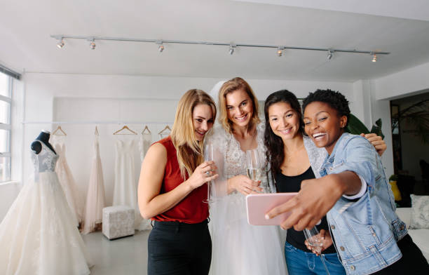 istock Bride with friends taking selfie in bridal boutique 908238108