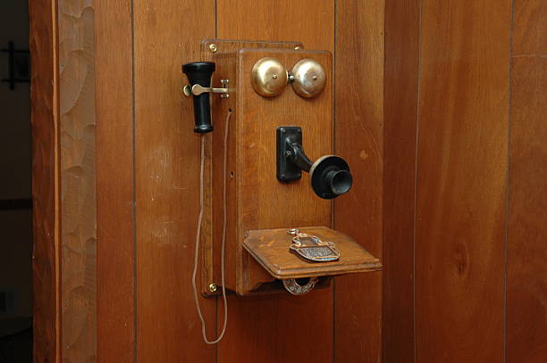 Antique wooden wall telephone with brass elements, mounted on a white wall.