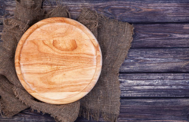 istock Round cutting board on old wooden texture background. Top view 908259172