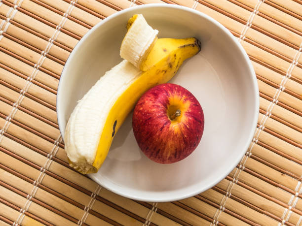 Closeup of two apple, a raspberry and a banana creating a happy face on a wood background.