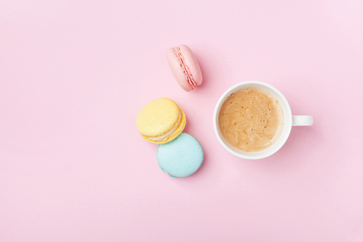 Cup of coffee and colorful macaron on pastel pink background top view. Cozy breakfast. Fashion flat lay.