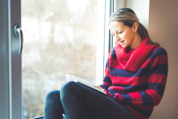 istock young beautiful woman with red and black pullover is reading book an windowsill 908293728