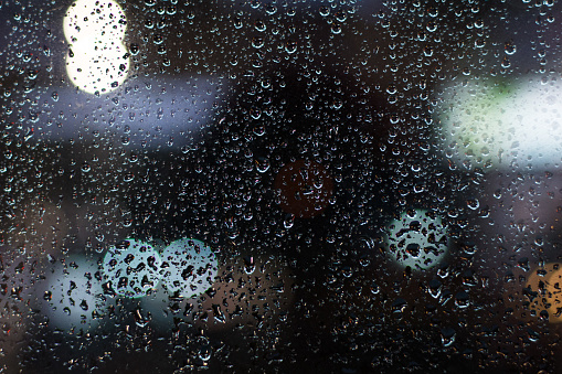 Rain drops on window glass at night with bokeh lights