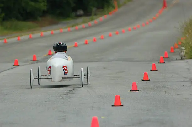 Young race car driver pilots a soap box derby car down the track. DOF focus placed directly on the racer while the lane and traffic cones that line it blur into the background.