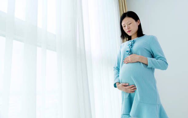 istock Pregnant woman standing by window 908323992