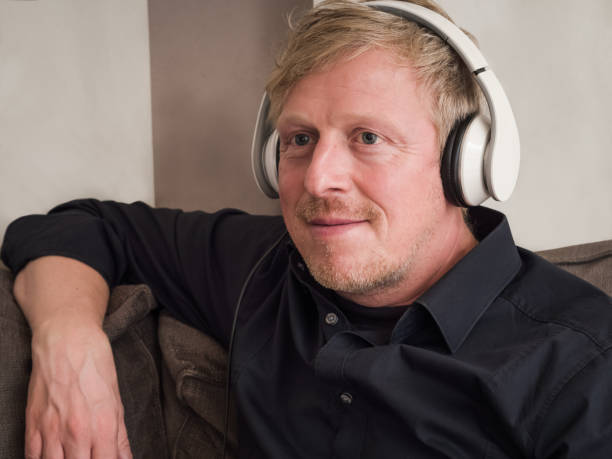 istock Mature man with white headphones on a couch. 908327408