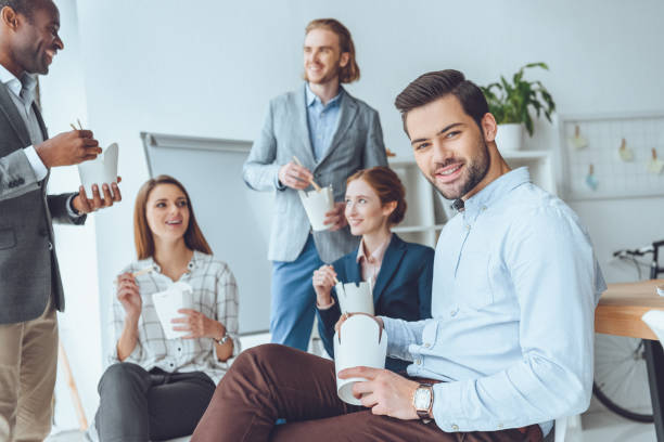 istock smiling businesspeople eating from paper boxes at office space 908327660