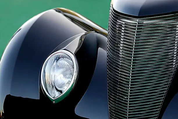 A close up view of a classic old Ford car showing only the front fender, headlight, and grill.