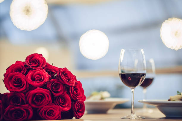 Romantic dinner in restaurant Romantic dinner settings. Two glasses of wine, dishes and bouquet of red roses are on table. rose bouquet red table stock pictures, royalty-free photos & images