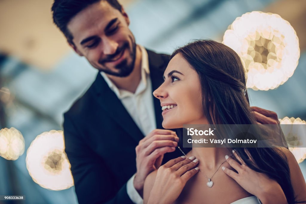 Romantic couple in restaurant Beautiful loving couple is spending time together in modern restaurant. Attractive young woman in dress and handsome man in suit are having romantic dinner. Celebrating Saint Valentine's Day. Jewelry Stock Photo