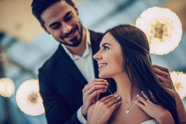 Romantic couple in restaurant Beautiful loving couple is spending time together in modern restaurant. Attractive young woman in dress and handsome man in suit are having romantic dinner. Celebrating Saint Valentine's Day. jewelry stock pictures, royalty-free photos & images