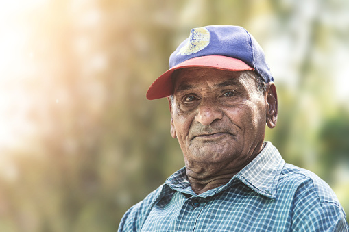 Elderly Indian seventy plus year old man outdoors in a home setting. looking directly at camera. Head and shoulders, one person, horizontal composition with copy space and selective focus.