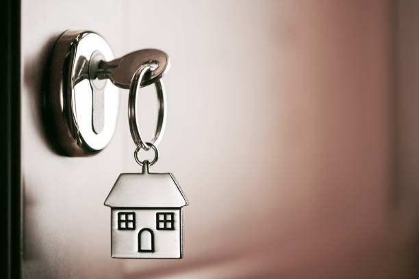 House key on a house shaped silver keyring in the lock of a entrance  brown door stock photo