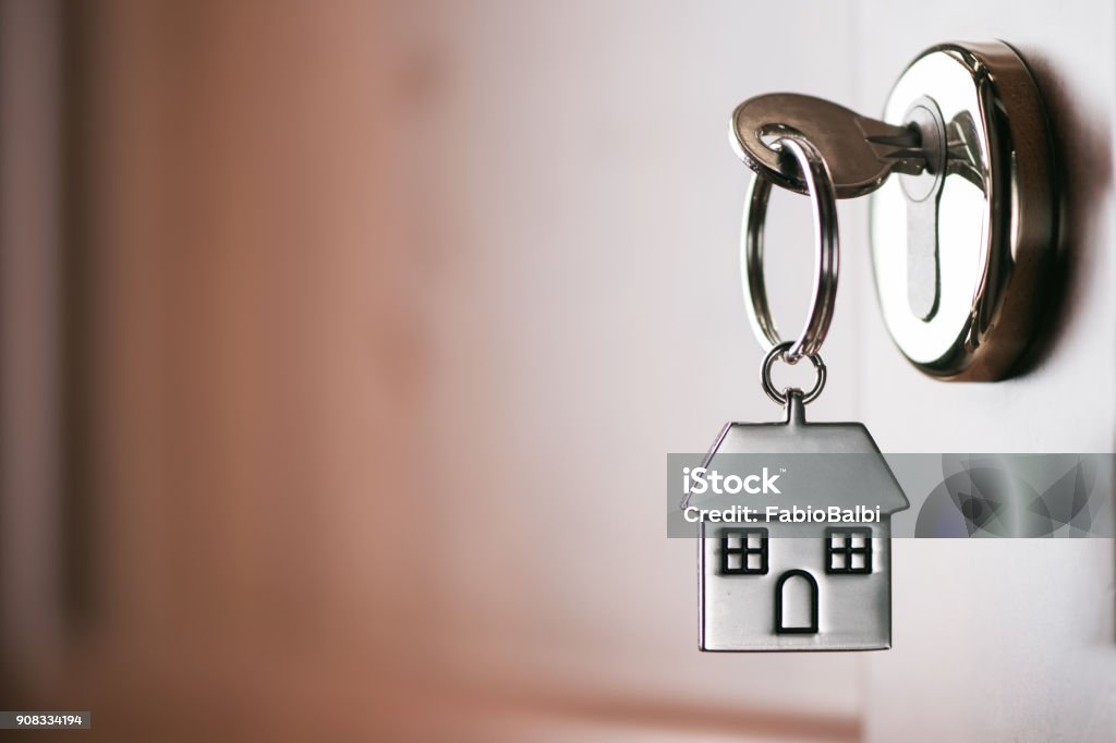 House key on a house shaped silver keyring in the lock of a entrance  brown door House key on a house shaped silver keyring in the lock of a door House Stock Photo
