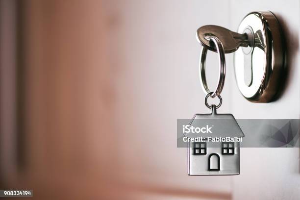 House Key On A House Shaped Silver Keyring In The Lock Of A Entrance Brown Door Stock Photo - Download Image Now