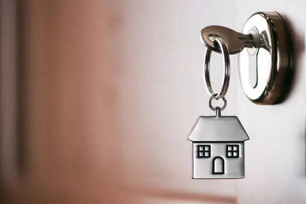 Photo of House key on a house shaped silver keyring in the lock of a entrance  brown door