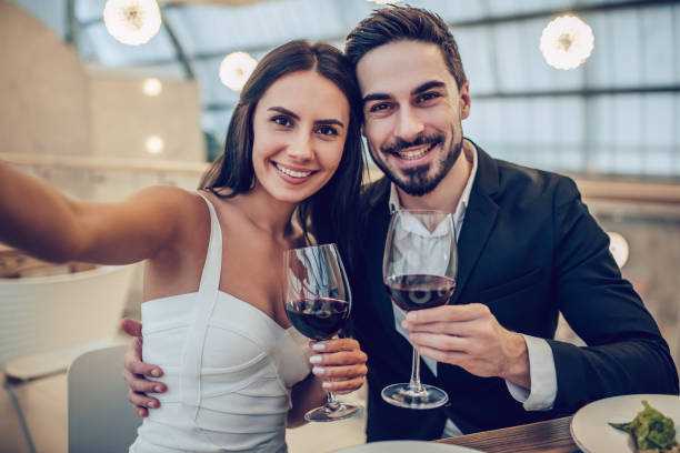 Romantic couple in restaurant Beautiful loving couple is spending time together in modern restaurant. Attractive young woman in dress and handsome man in suit are having romantic dinner. Celebrating Saint Valentine's Day. well dressed stock pictures, royalty-free photos & images