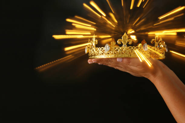 istock Woman's hand holding a crown for show victory or winning first place over black background with glitter overlay. 908344454