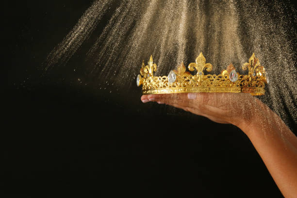 istock Woman's hand holding a crown for show victory or winning first place over black background with glitter overlay. 908344456