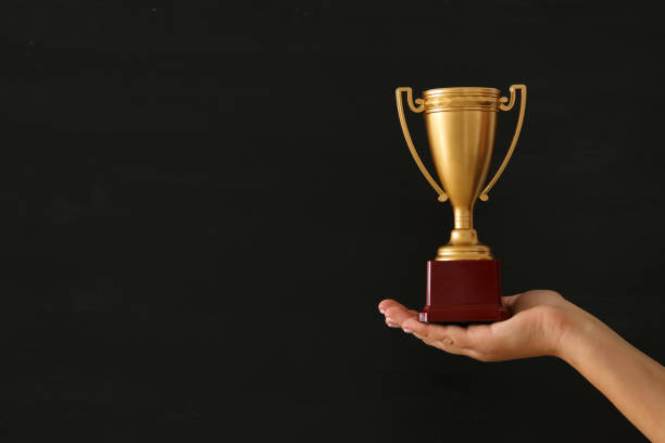 istock low key image of a woman holding a trophy cup over dark background. 908344552
