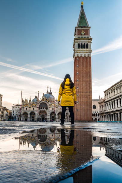 istock Young woman, in yellow raincoat seen from back at St. Mark square 908356452