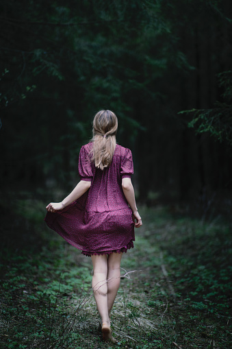 Barefoot girl walks through a dark forest