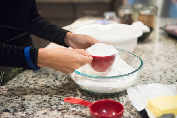 Young Woman Baking at Home Measures Flour Ingredient This is a color, royalty free photograph of a young 20 year old Millennial woman baking cupcakes from scratch at home in the kitchen in Orlando, Florida, USA. She measures out a cup of flour to add to the batter ingredients. Cup of Flour stock pictures, royalty-free photos & images