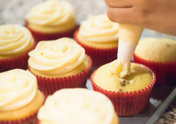 This is a color, royalty free photograph of a full tray of freshly baked homemade cupcakes being topped with vanilla icing in Orlando, Florida, USA