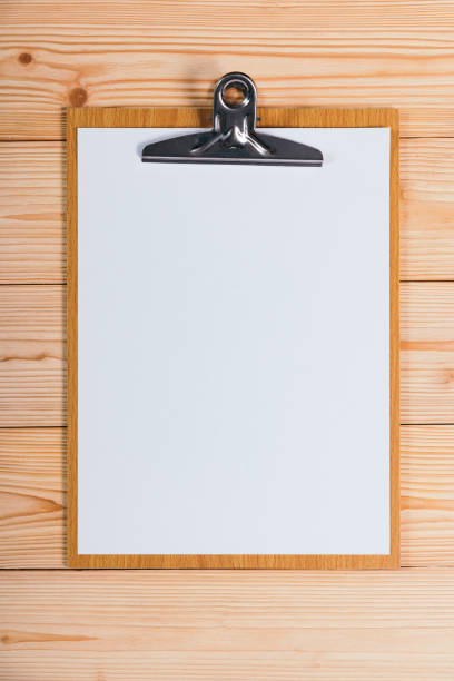 istock clipboard with blank white paper sheet on wood table top view with copy space. 908483886