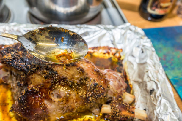closeup spoon with juice sauce over cooked lamb leg joint on roasting tin foil ready for serving - lamb shank dinner meal imagens e fotografias de stock