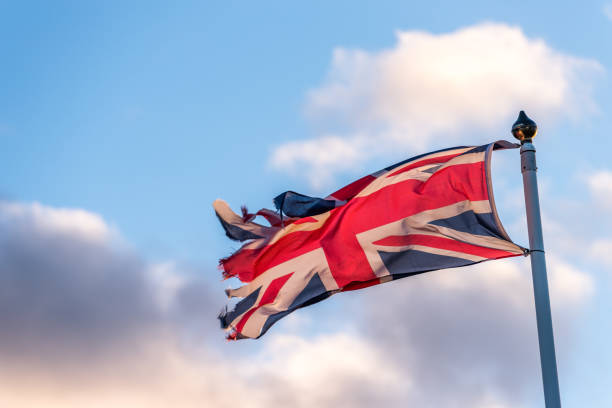 istock British Flag with torn edges waving over cloudy sky 908506200