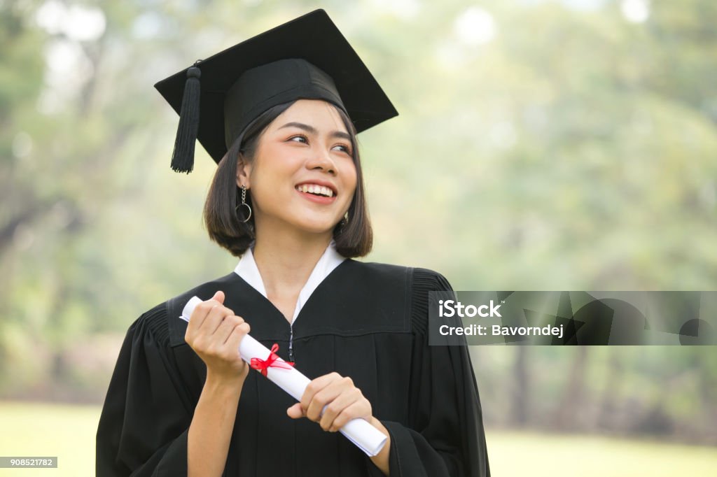 若いアジアの女子学生は、卒業の帽子とガウン、庭の背景、卒業の概念を持つ女性を身に着けています。 - 卒業式のロイヤリティフリーストックフォト