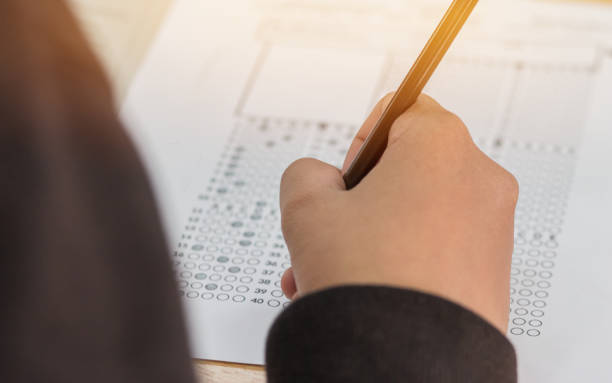 istock high school or university student hands taking exams, writing examination on paper answer sheet optical form of standardized test on desk doing final exam in classroom. Education  literacy concept. 908524952