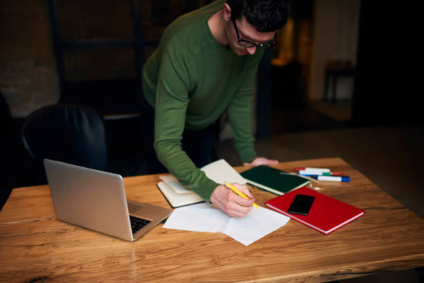 istock Concentrated male editor of newspaper preparing article working with documentation checking mistakes in text working overtime in coworking space using laptop computer and free wireless connection 908550070
