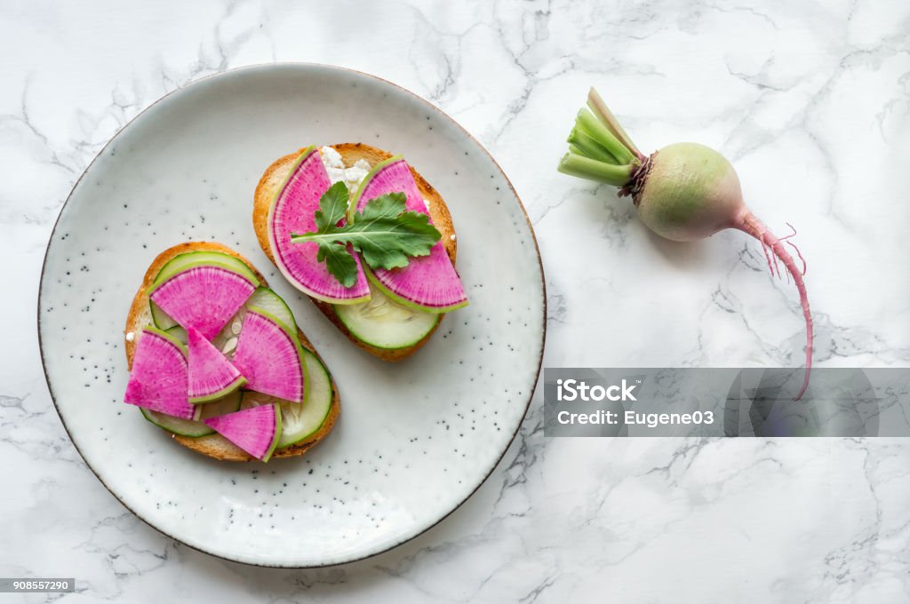 Detox fresh vegetables food. Healthy toast made from sliced watermelon radish (chinese daikon), cucumber and rucola on marble table. Top view. Healthy Eating Stock Photo