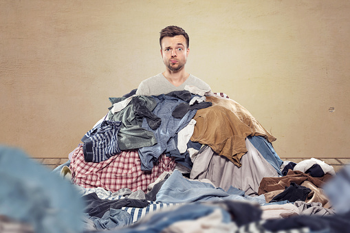 A man is covered by a heap of clothes. Funny and confused expression on his face.