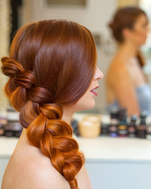 linda garota com longos cabelos vermelhos, trançado com uma trança francesa, em um salão de beleza. - braided braids women long hair - fotografias e filmes do acervo