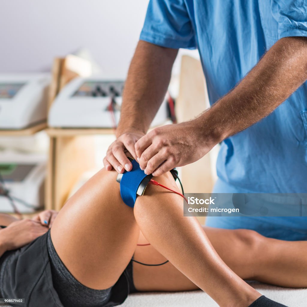 Electrical stimulation in physical therapy. Therapist positioning electrodes on a patient's knee Physical Therapy Stock Photo