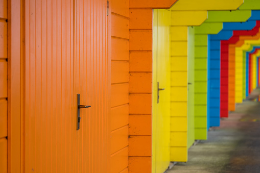 Row of abstract rainbow colored beach house chalet pavilions on the east coast of England in a popular seaside resort, with relections in puddles of water on the ground.