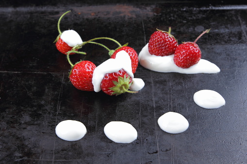 Fresh strawberries with cream on a dark background, red berries with sour cream on the old surface, forest berries and dairy products, healthy food, sour-milk products, vegan, fruit in minimalism style