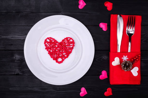 istock Valentines day table setting with fork, knife, plate and red dinner napkin on black background. 908583570