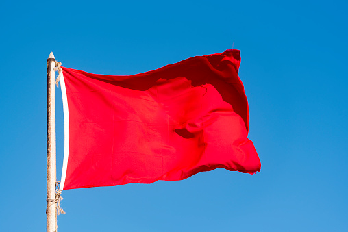 Old red flag and blue sky, red banner waving against blue sky