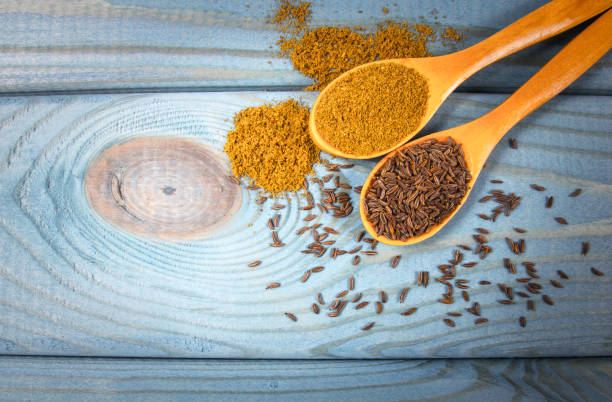 Ground cumin in a spoon and whole cumin on the wooden background. stock photo